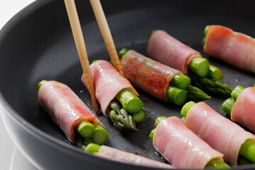 フライパンでアスパラベーコンを焼く料理のシーン　Asparagus Bacon Being Cooked in a Frying Pan