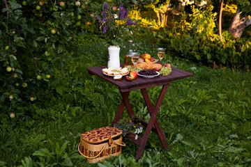 Romantic picnic table setting with wine, fruits, bread and wildflowers in garden