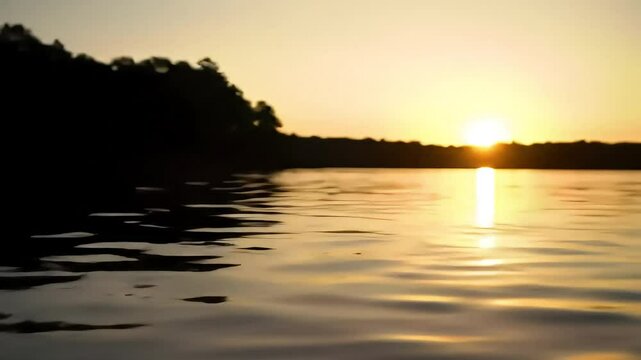 Dark water ripples with a blurred treeline  sunset glow in the background