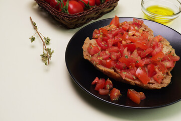 Frisella condita con pomodoro, olio. e origano, cotola di pomodorini e rametto di origano sul tavolo