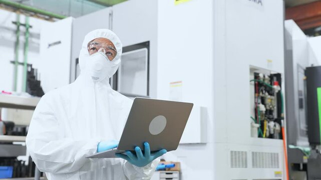 A male worker wearing protective clothing working in a factory with a laptop