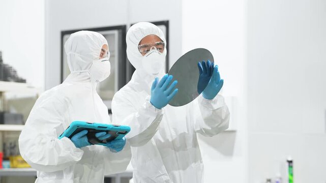 半導体工場でタブレットを持ってシリコンウエハーを検査する防護服を着た男女作業員