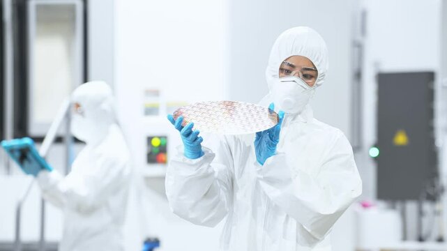 A female worker in protective clothing inspects silicon wafers in a semiconductor factory