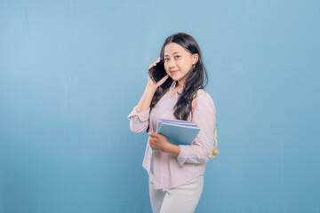 Fototapeta premium A woman is talking on her cell phone while holding a stack of books. She is smiling and she is in a good mood