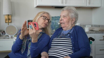 A daughter helps her elderly mother connect with family through a smartphone, capturing precious memories and fostering love and support in their cozy home.