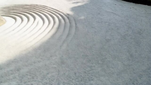 Tranquil zen garden scene featuring raked white sand with circular patterns around large rocks, contrasted with patches of green moss