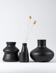 minimalist matte pale modern black vases of various shapes lined up on a white background