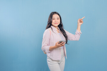 A woman is a holding a cell phone and pointing to something important. She is smiling and she is...