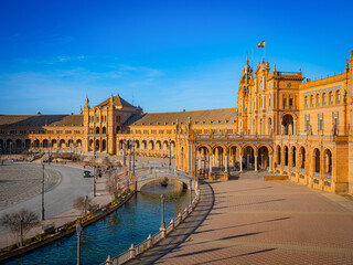 Fototapeta premium Majestic Plaza de España in Seville, Spain, features ornate Renaissance Revival architecture, colorful tiles, and a serene canal under a radiant blue sky.