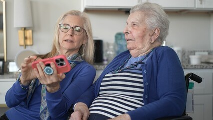 A woman in her 90s enjoys a video chat with her daughter. They share joyful memories while sitting...