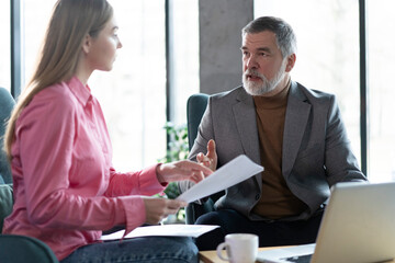 Professional mature businessman and businesswoman colleagues sitting in office having business...