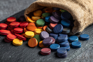Colorful wooden tokens spilling from a burlap sack on a dark slate background during a crafting session
