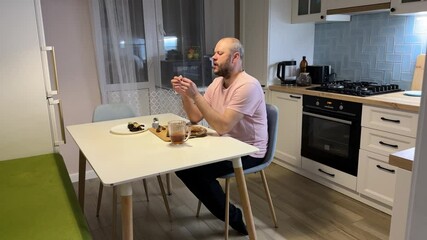 In the kitchen, an adult male is sipping beer and eating dried fish.