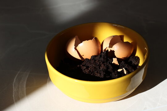 Yellow bowl with coffee grounds and egg shells on marble kitchen table with deep shadows and sun light, minimalistic style. 
