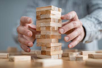 Hands carefully balancing wooden blocks in a strategic game in a bright indoor space during afternoon light