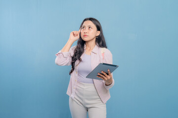 Fototapeta premium A woman is holding a tablet and looking up at the ceiling. She is deep in thought