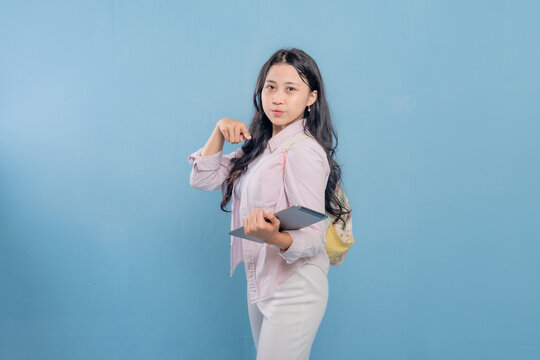 A woman is holding a tablet and pointing at something. She is wearing a pink shirt and white pants