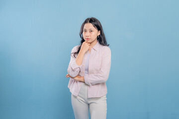 A woman is standing in front of a blue wall, wearing a pink jacket and white pants. She is looking...