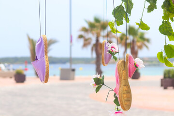 Vibrant flip-flops hanging from a string with flowers against a backdrop of the Mediterranean coast...