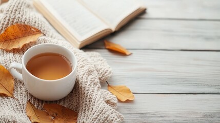 A warm cup of tea sits beside a book and autumn leaves on a soft blanket, capturing a cozy and inviting atmosphere perfect for relaxation and introspection.