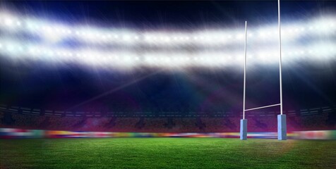 White rugby goal posts standing right side on floodlit green pitch, tiered seating, rain falling