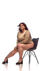 A plus-size woman confidently poses on a chair in an editorial style outfit with bold visual...