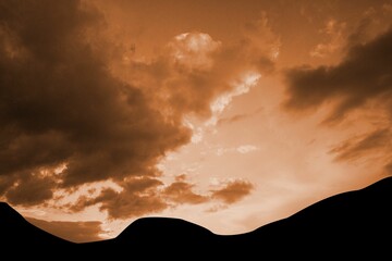 Silhouette of rolling dunes is spanning width in minimalist flat design, with warm glowing clouds