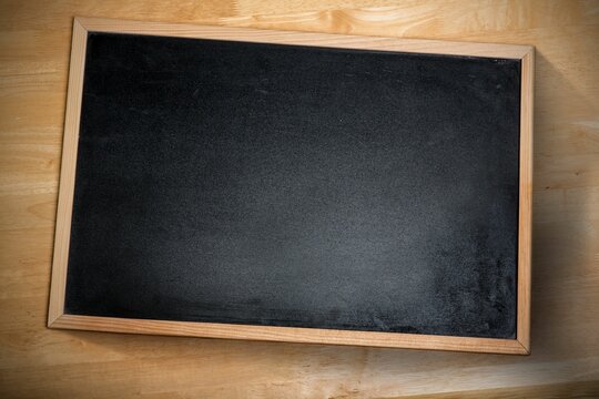 Fototapeta Framed blackboard is resting diagonally on wood-grain tabletop, under soft overhead light