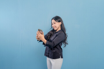 A woman is looking at her phone while standing in front of a blue wall. She is smiling and happy by something on her phone