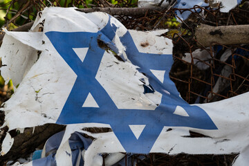 Remnants of a torn and tattered blue and white flag of the State of Israel clinging to a chainlink...