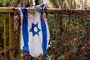 Wet, wrinkled and tattered flag of the State of Israel hanging from a metal railing in a rain storm.