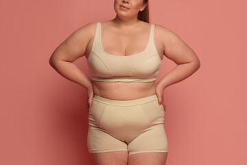 A confident Caucasian woman in comfortable underwear embraces body diversity against a pink...