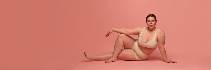 Obraz premium A confident woman in comfortable underwear celebrates body positivity against a soft pink background. Concept of self-acceptance and empowerment. Flyer, banner