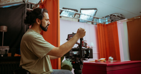 Director of photography with a camera in his hands on the set. Professional videographer at work on filming a movie, commercial or TV series. Filming process indoors, studio