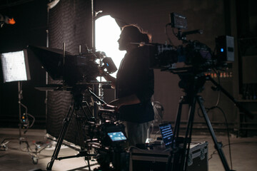 The director of photography with a camera on the set. A professional videographer is working on filming a movie or commercial for a TV series. The filming process takes place indoors in a studio.