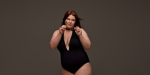 A plus-size woman confidently poses in a stylish black swimsuit, embracing body positivity and...