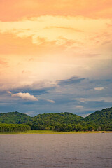 A peaceful rural scene in the dam featuring a yellow meadow and green mountain with blue sky, Chachoengsao, Thailand.