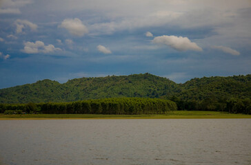 A peaceful rural scene in the dam featuring a yellow meadow and green mountain with blue sky, Chachoengsao, Thailand.
