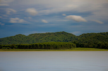 A peaceful rural scene in the dam featuring a yellow meadow and green mountain with blue sky, Chachoengsao, Thailand.