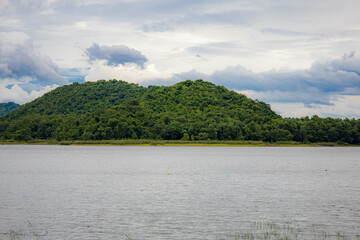 A peaceful rural scene in the dam featuring a yellow meadow and green mountain with blue sky, Chachoengsao, Thailand.