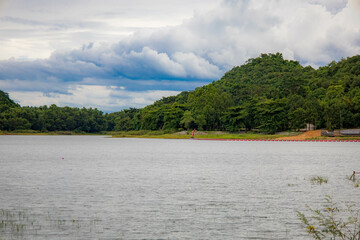 A peaceful rural scene in the dam featuring a yellow meadow and green mountain with blue sky, Chachoengsao, Thailand.