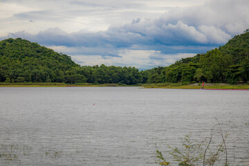 A peaceful rural scene in the dam featuring a yellow meadow and green mountain with blue sky, Chachoengsao, Thailand.