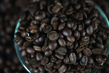 Aromatic Brew: Roasted coffee beans cascade from a glass container, their rich, dark brown hues a feast for the senses. Captured from a high angle.