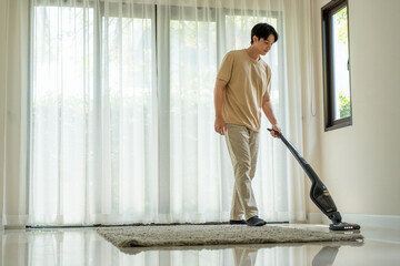 Asian male  is vacuuming the house with a cordless vacuum cleaner.
