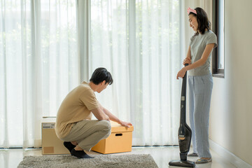 Couple of Asian people help together for unpack box re arrange home decor while woman clean the...