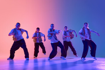 An energetic dance group performs under vibrant, colorful lighting in an urban dance studio....