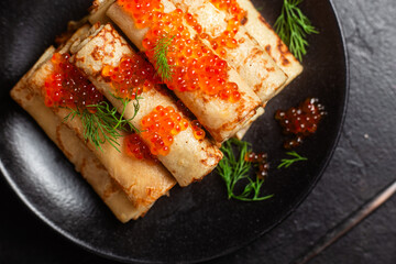 Delicious blini with red caviar in a black plate on the table. Thin pancakes. 