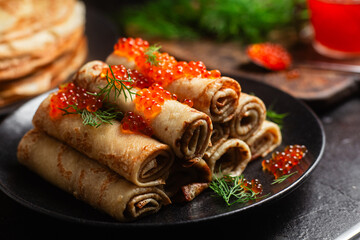 Delicious blini with red caviar in a black plate on the table. Thin pancakes. 