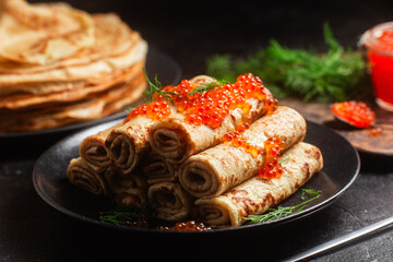 Delicious blini with red caviar in a black plate on the table. Thin pancakes. 