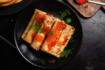 Delicious blini with red caviar in a black plate on the table. Thin pancakes. 